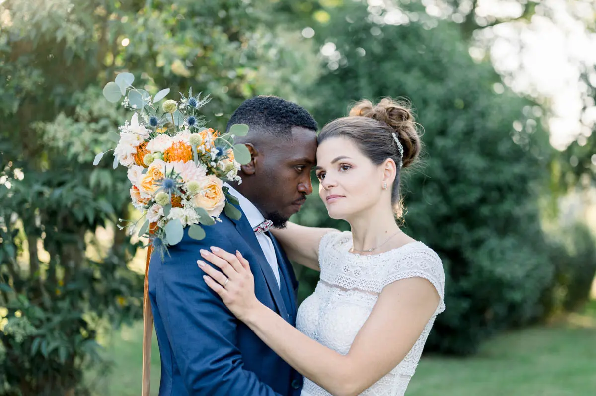 The couple embracing cheek to cheek, orange bouquet in hand