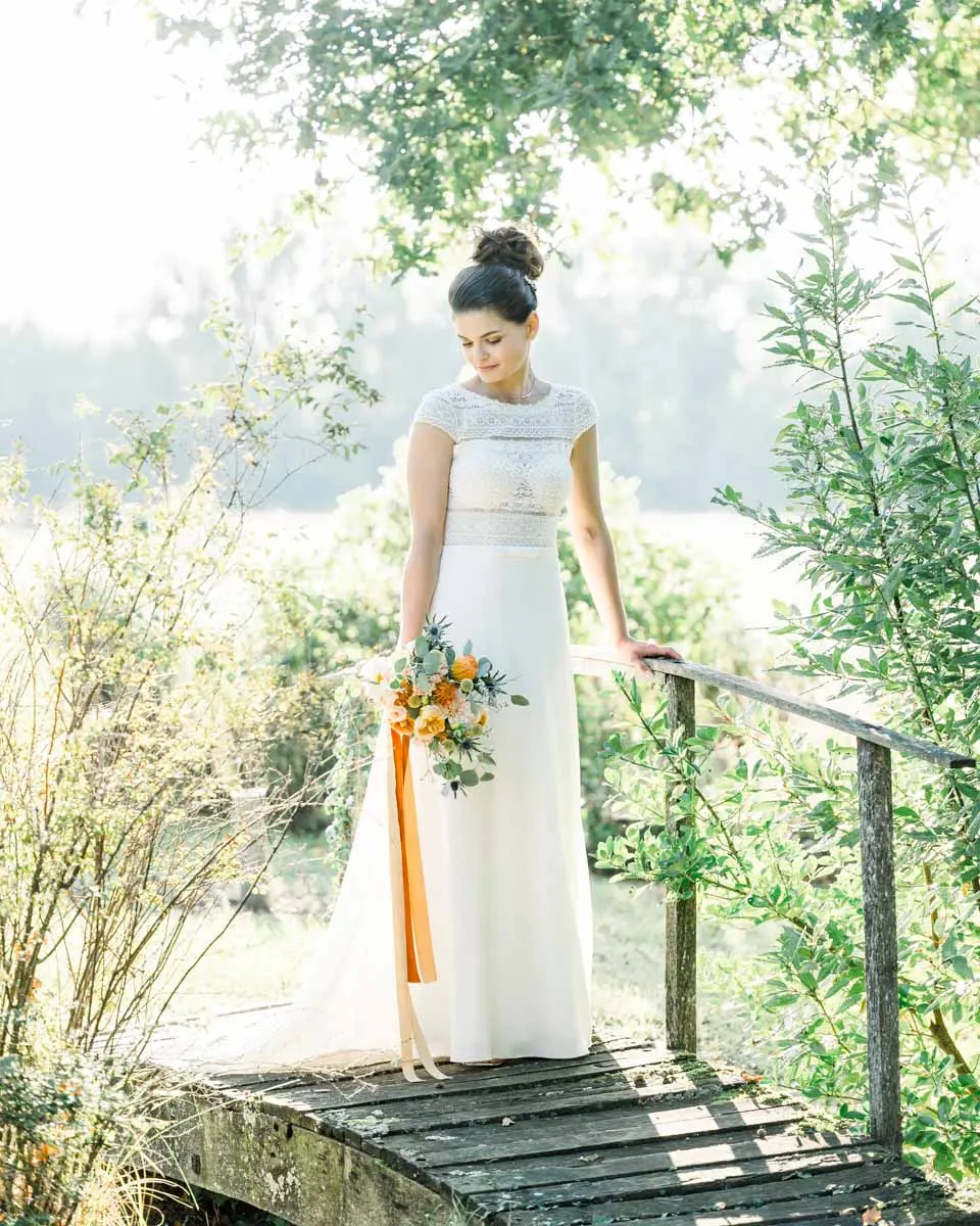 The bride on a small wooden footbridge surrounded by greenery