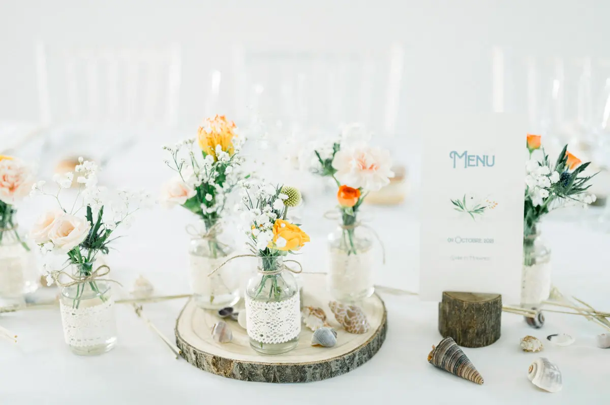 Small flower vases and a menu on a log slice, with seashell decorations