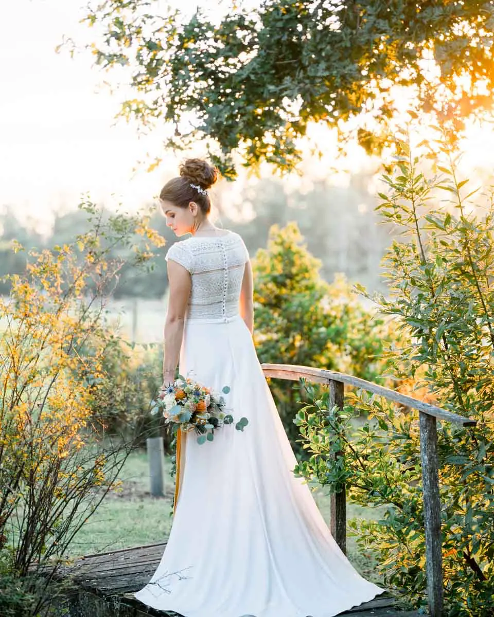 The bride seen from behind on the wooden footbridge in golden evening light