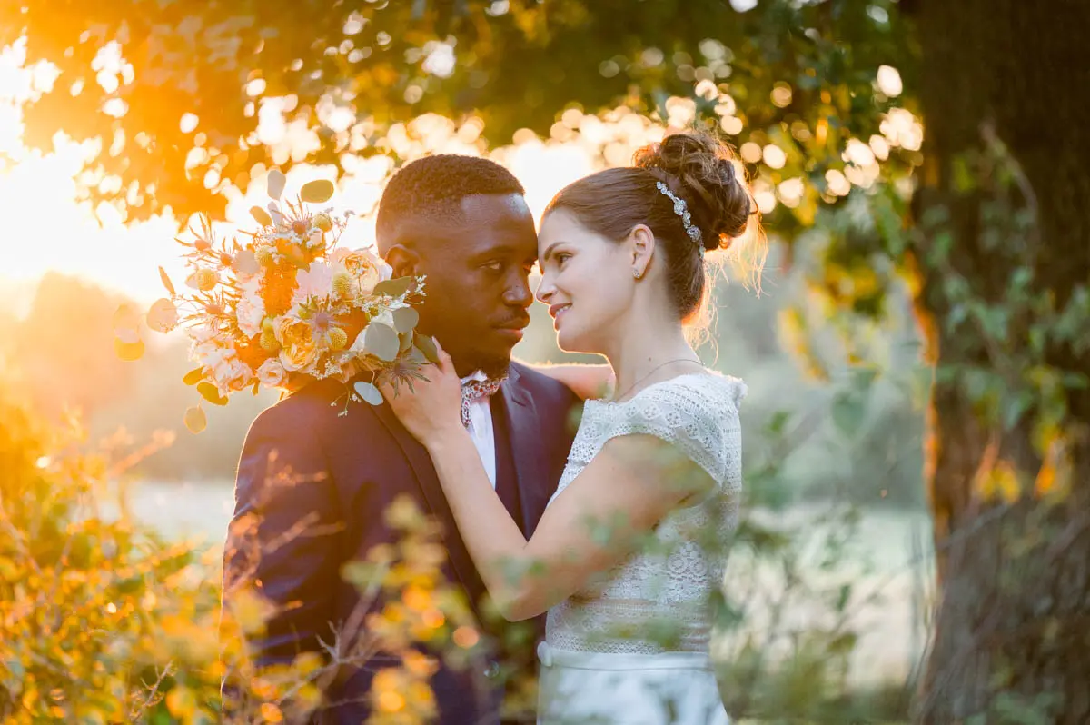 The bride with her hand on the groom's cheek under a tree at sunset
