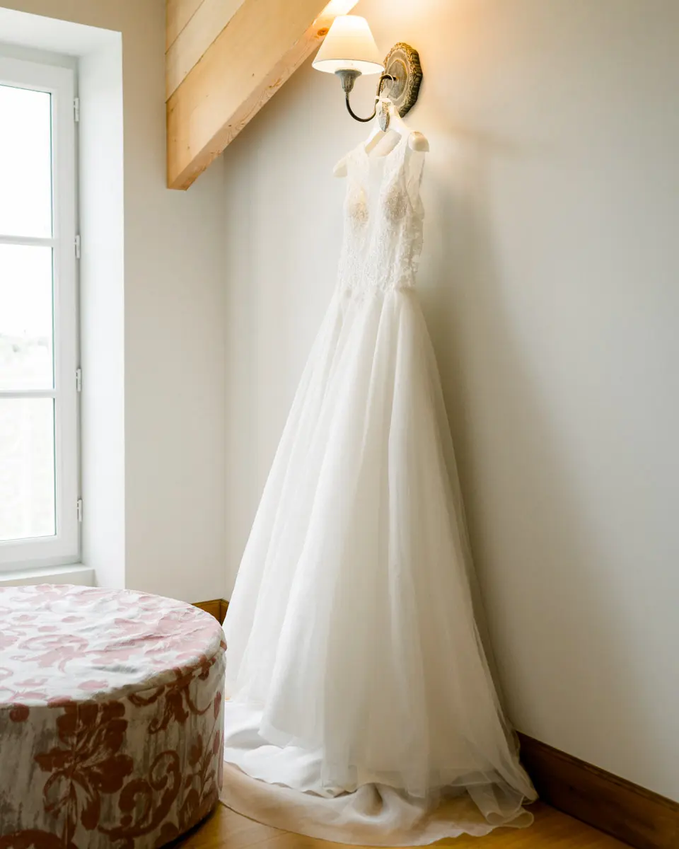 Wedding dress hanging by the window of a bright bedroom