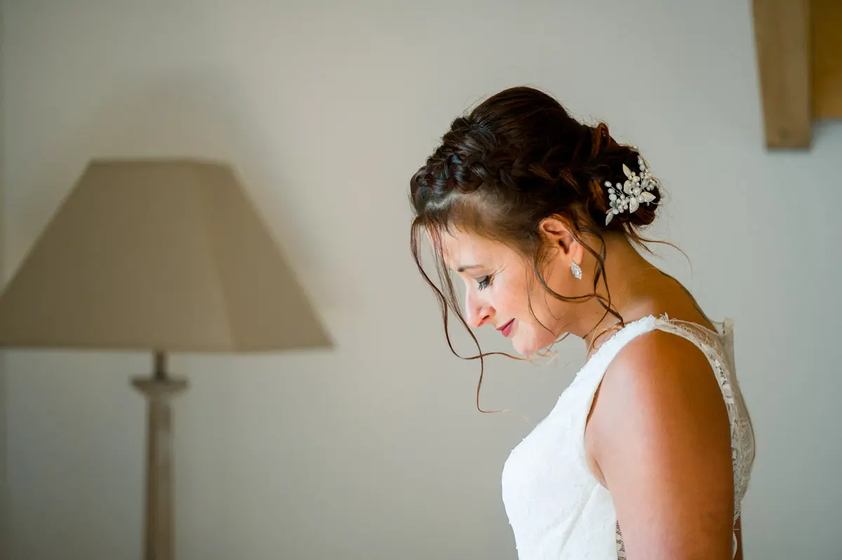 Bride with a pearl-adorned chignon looking down beside a lamp