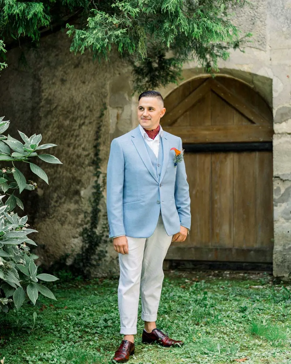 Groom in a sky-blue suit before an arched wooden door