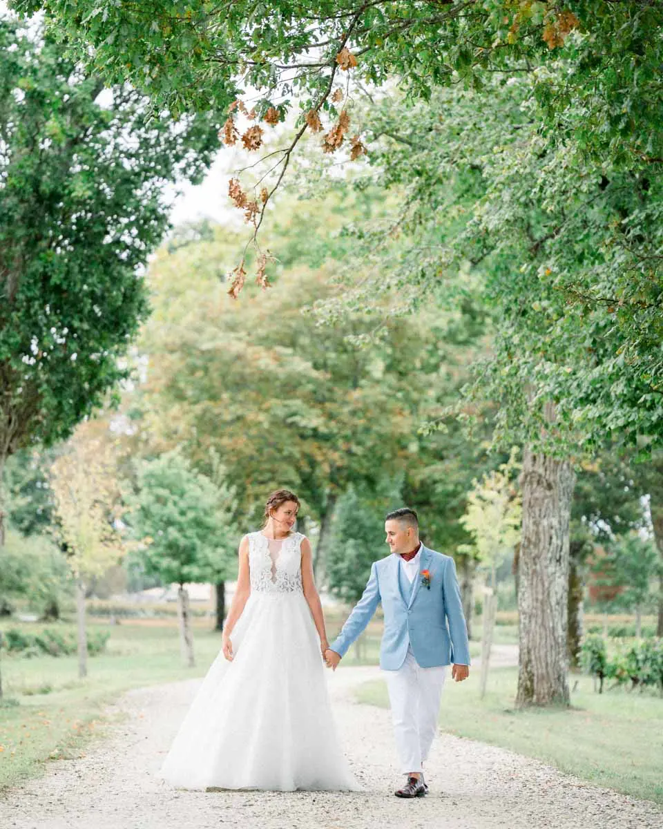 Laetitia and Anthony walking hand in hand under the trees of Château Duplessis