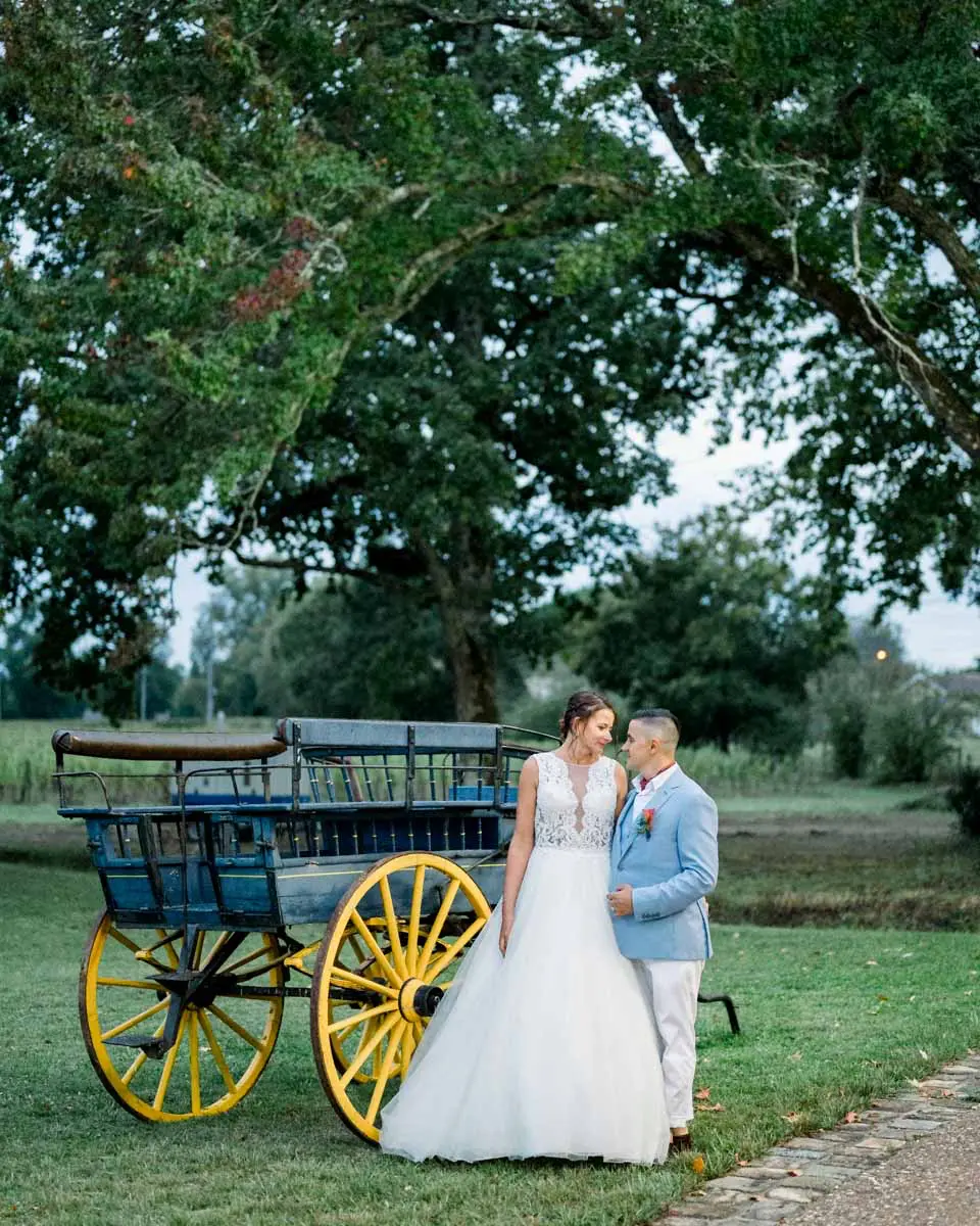 Bride and groom beside an old cart with yellow wheels in the park