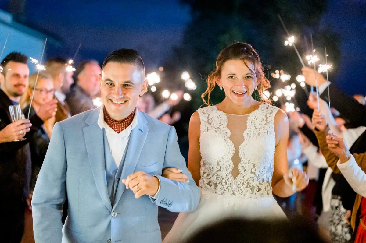 Smiling newlyweds walking between guests holding sparklers