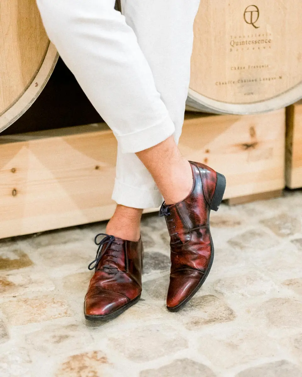 Groom's burgundy leather shoes crossed in front of wine barrels