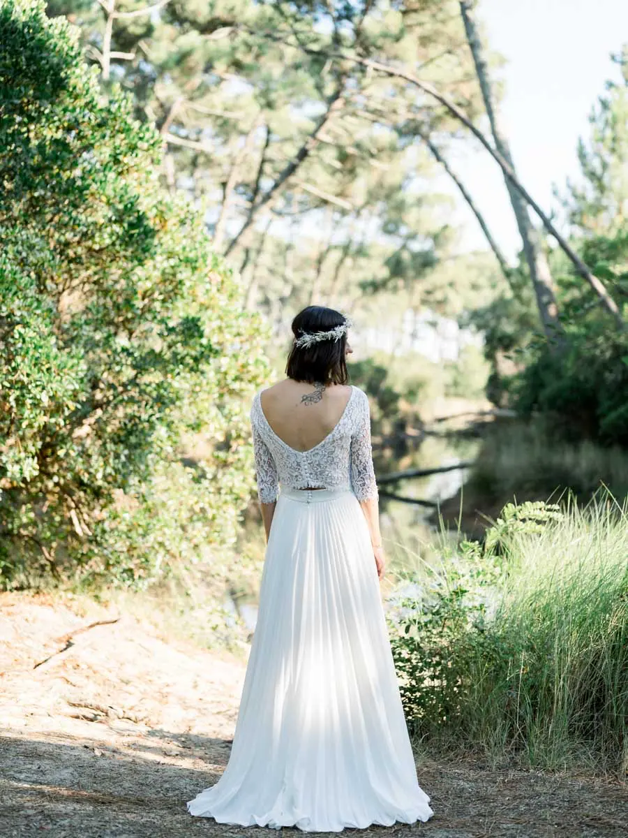 The bride seen from behind in her lace gown on a path beneath the pines