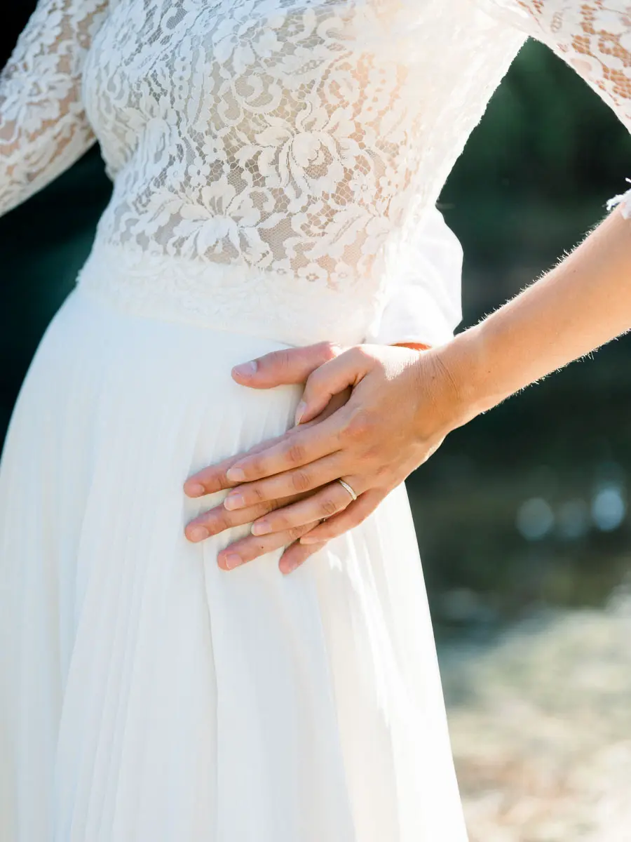 The groom's hands resting on the bride's lace gown