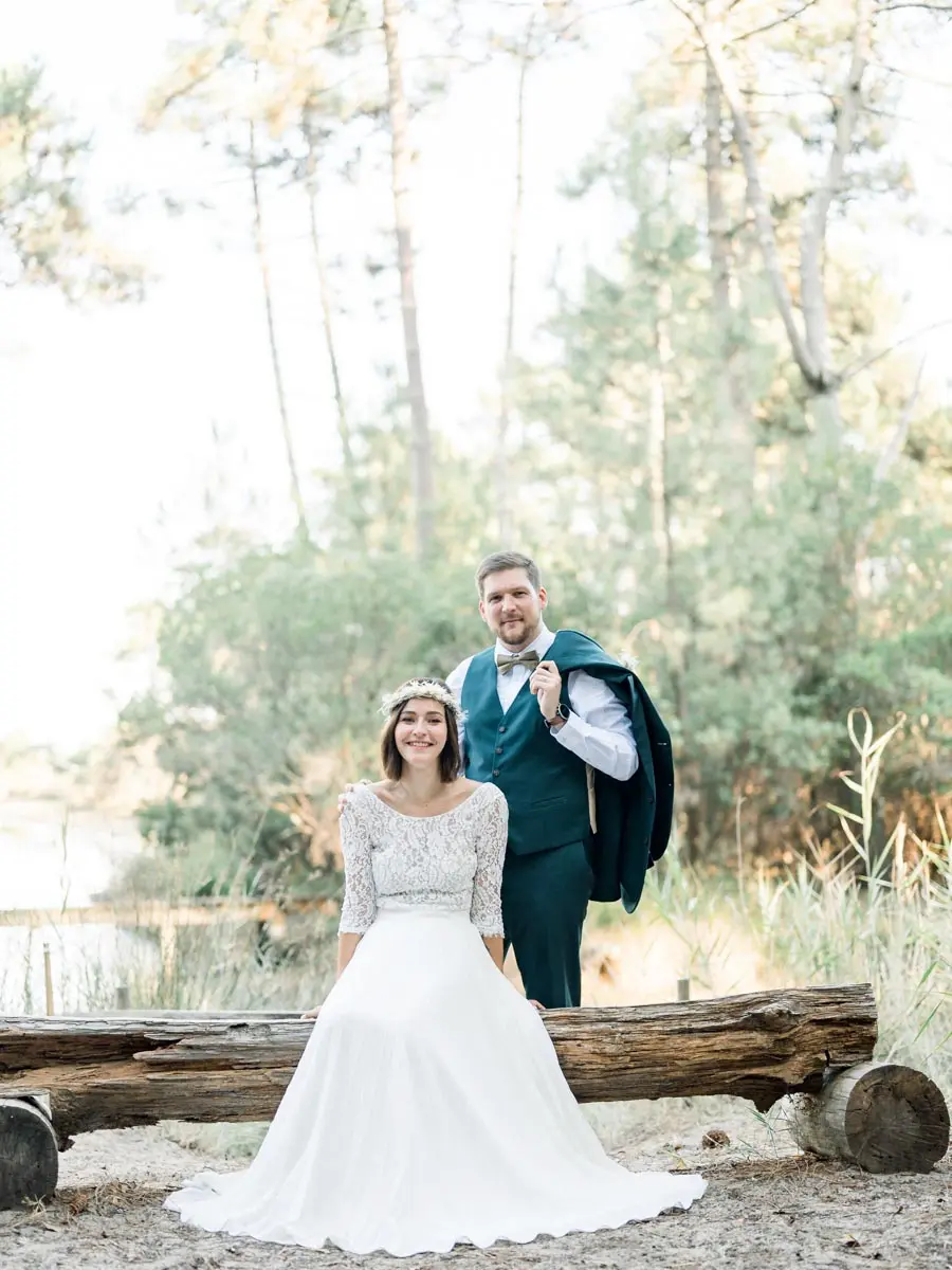 The groom with his jacket over his shoulder behind the bride by a fallen log