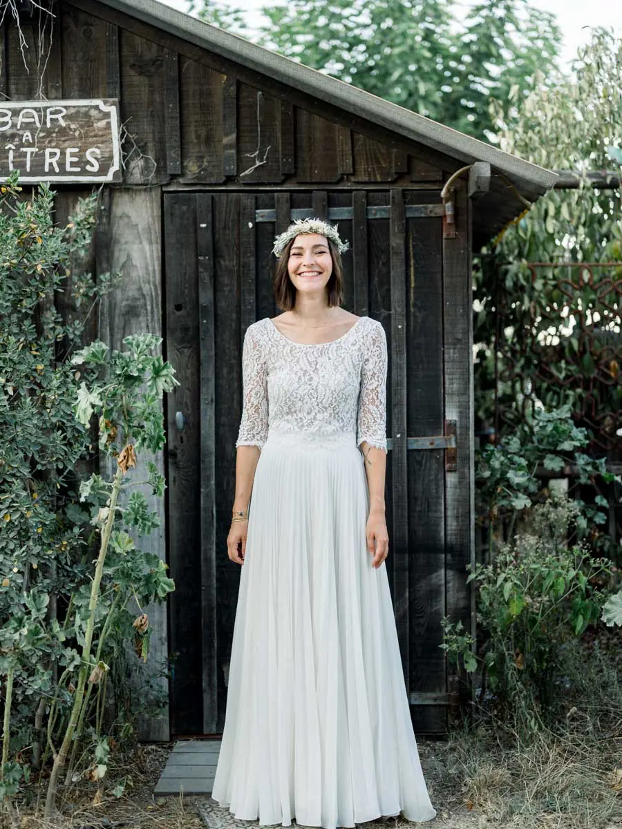 The smiling bride in front of a dark wooden hut