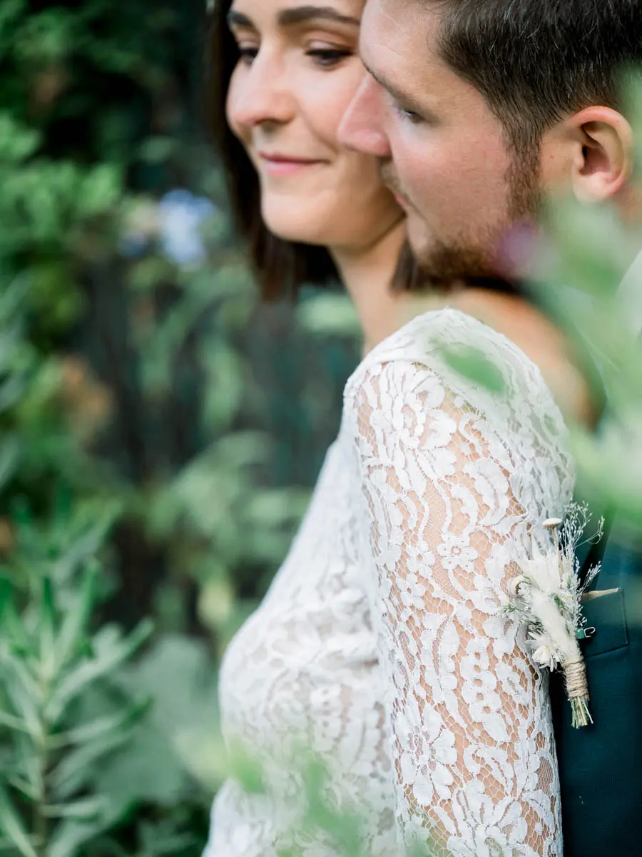 The newlyweds cheek to cheek, seen through foliage