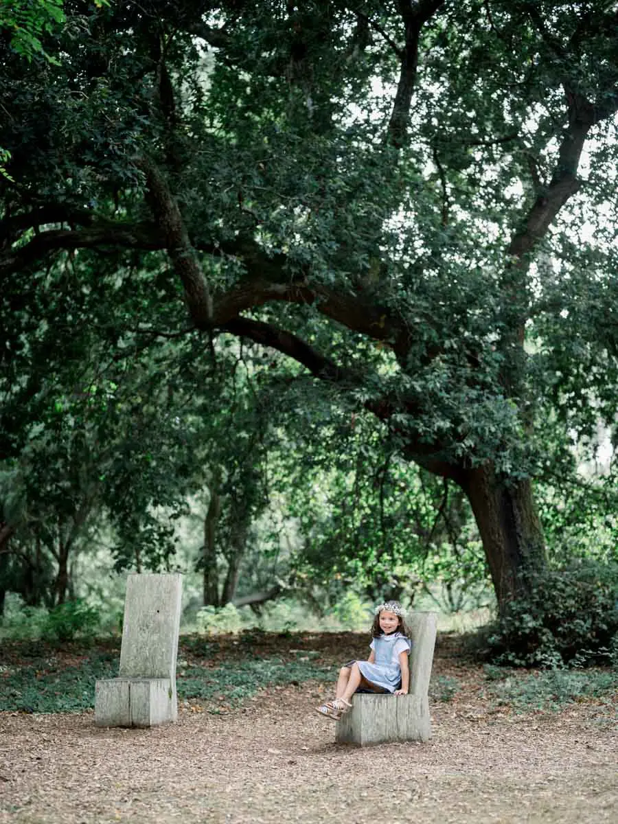 Little girl sitting on a wooden seat beneath a large oak