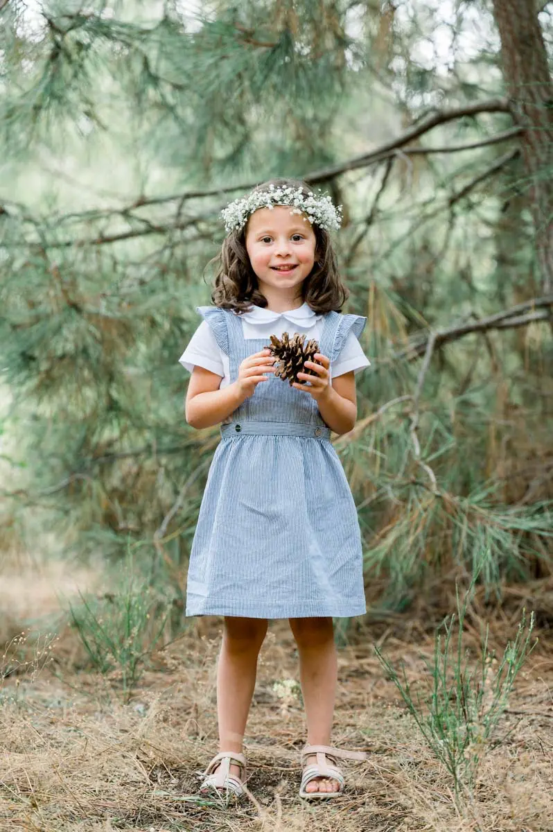 Girl in a blue dress and flower crown holding a pine cone