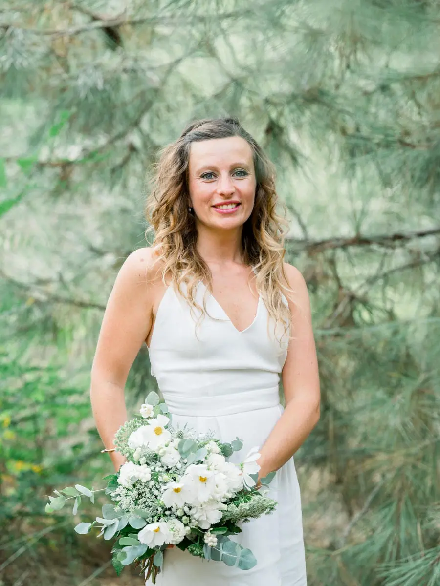 Mother in a white dress holding a white flower bouquet among the pines