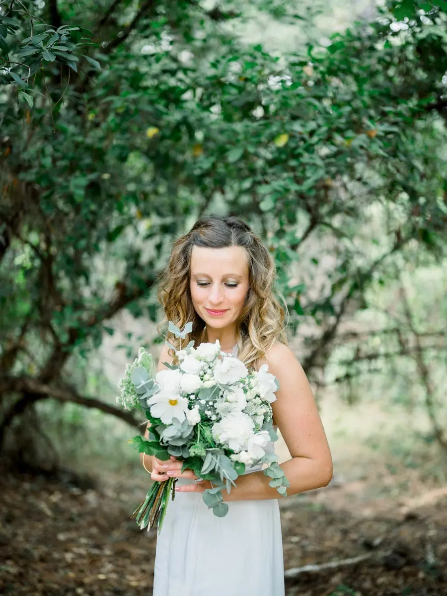 Mother smiling with a white flower bouquet in hand beneath the trees