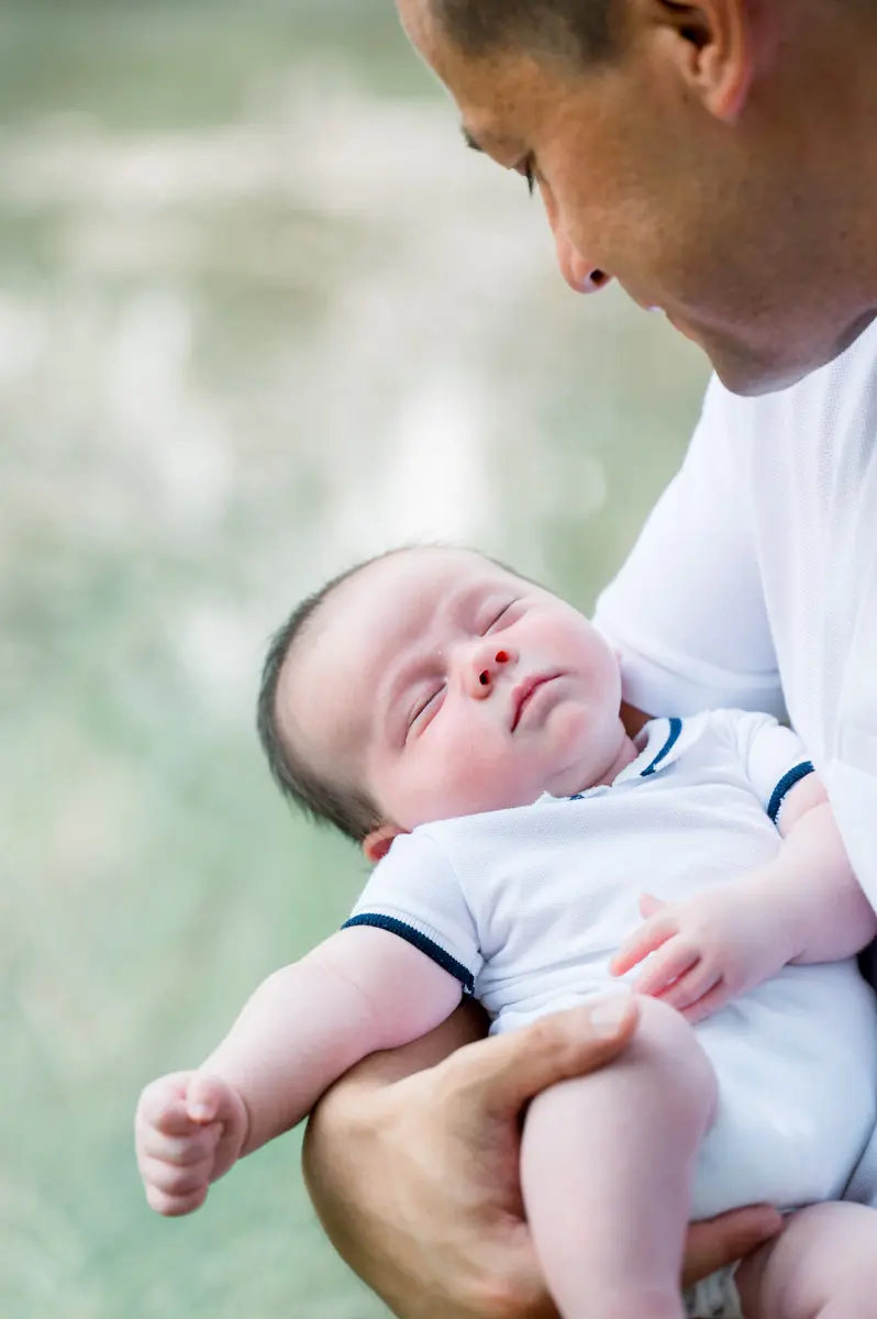 Newborn baby asleep in his father's arms outdoors