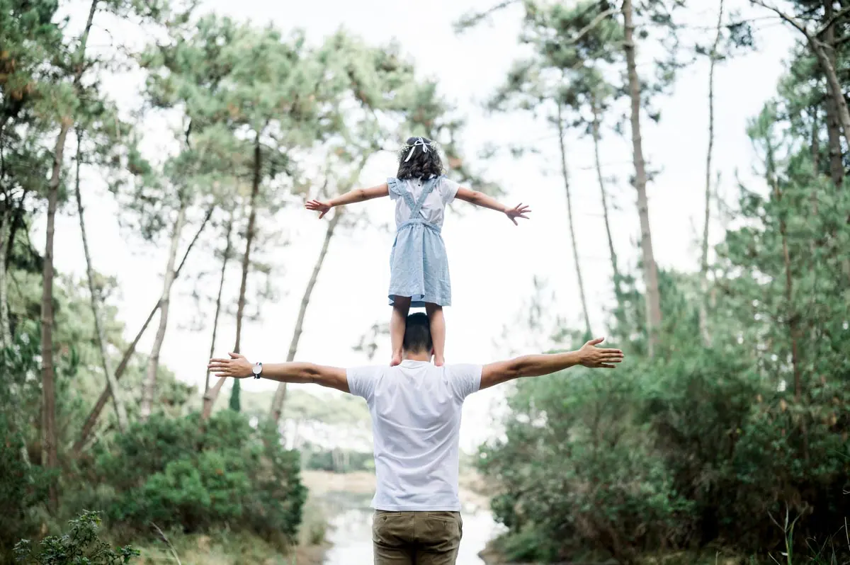 Girl standing on her father's shoulders, arms outstretched