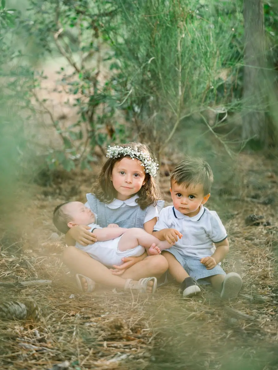 Three children sitting together on pine needles, including a baby