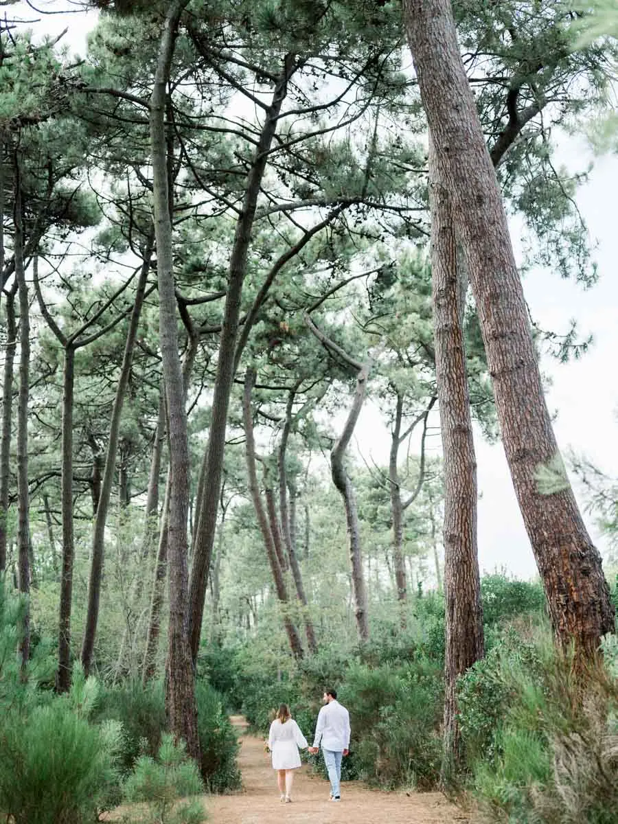 Expectant couple walking in the distance along a path through the pines of Arcachon Bay