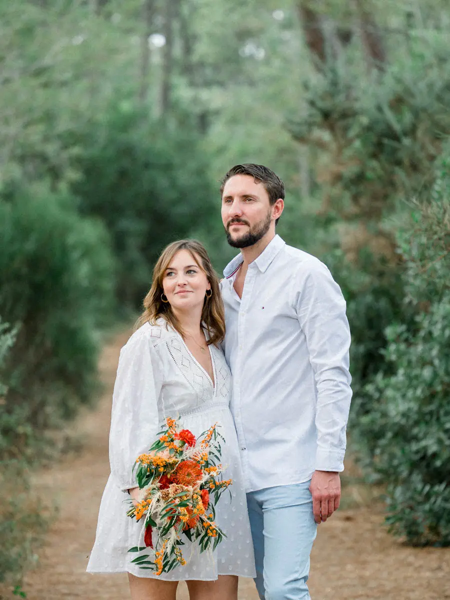 Mum-to-be in a white dress with an orange bouquet beside her partner on a path