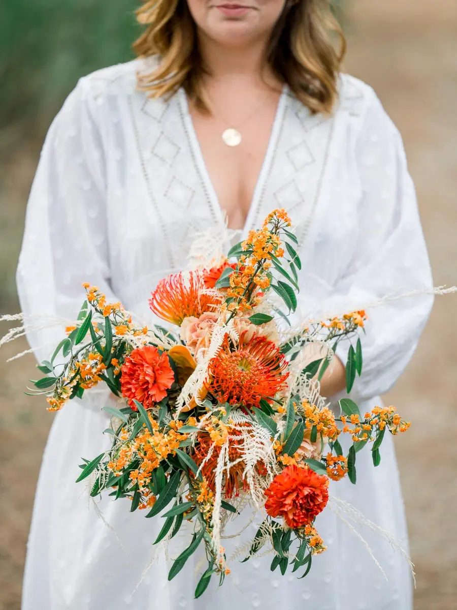 Orange and red flower bouquet held by the mum-to-be in a white dress