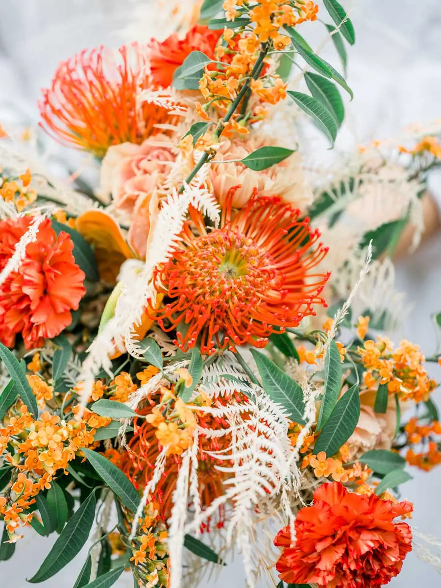 Close-up of the bouquet of proteas, orange roses and dried foliage