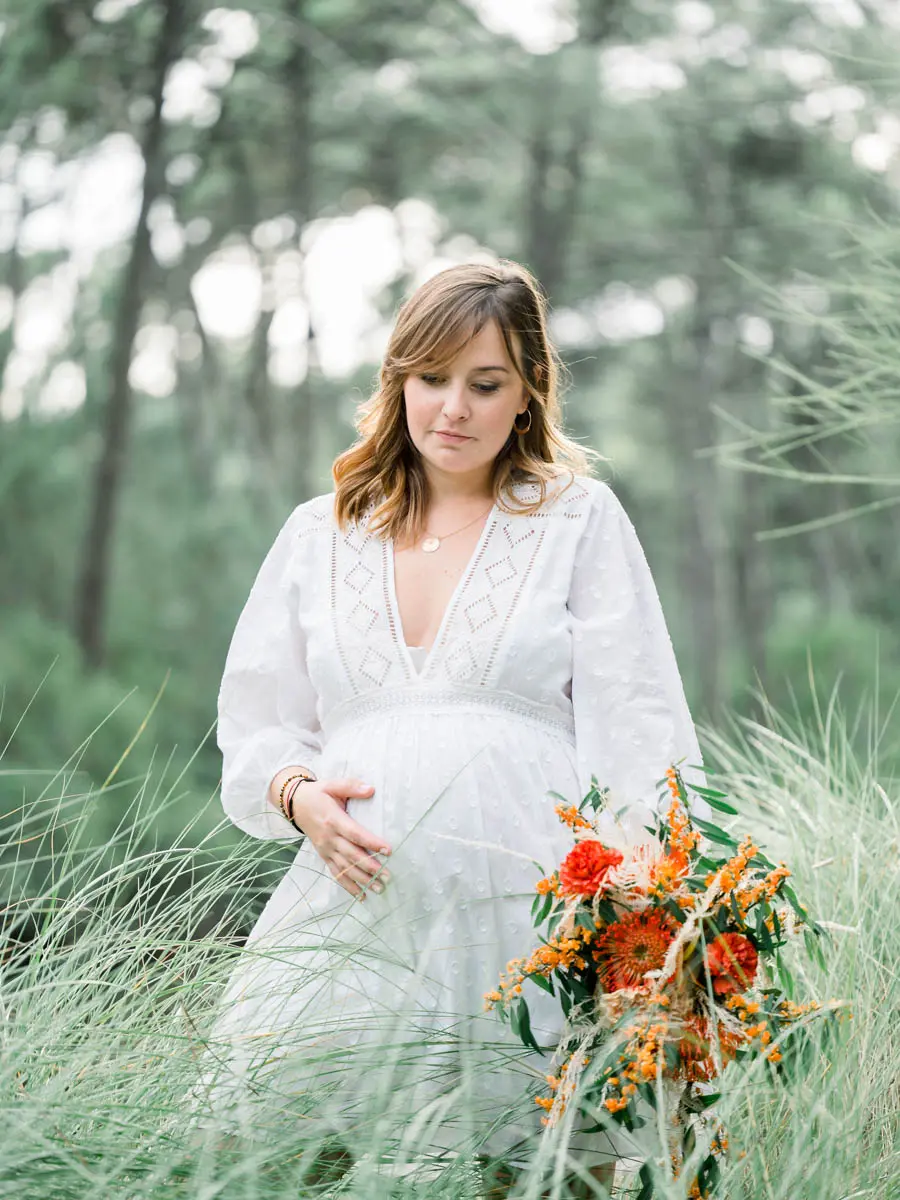 Mum-to-be in a white dress, hand on her bump, standing in tall grass