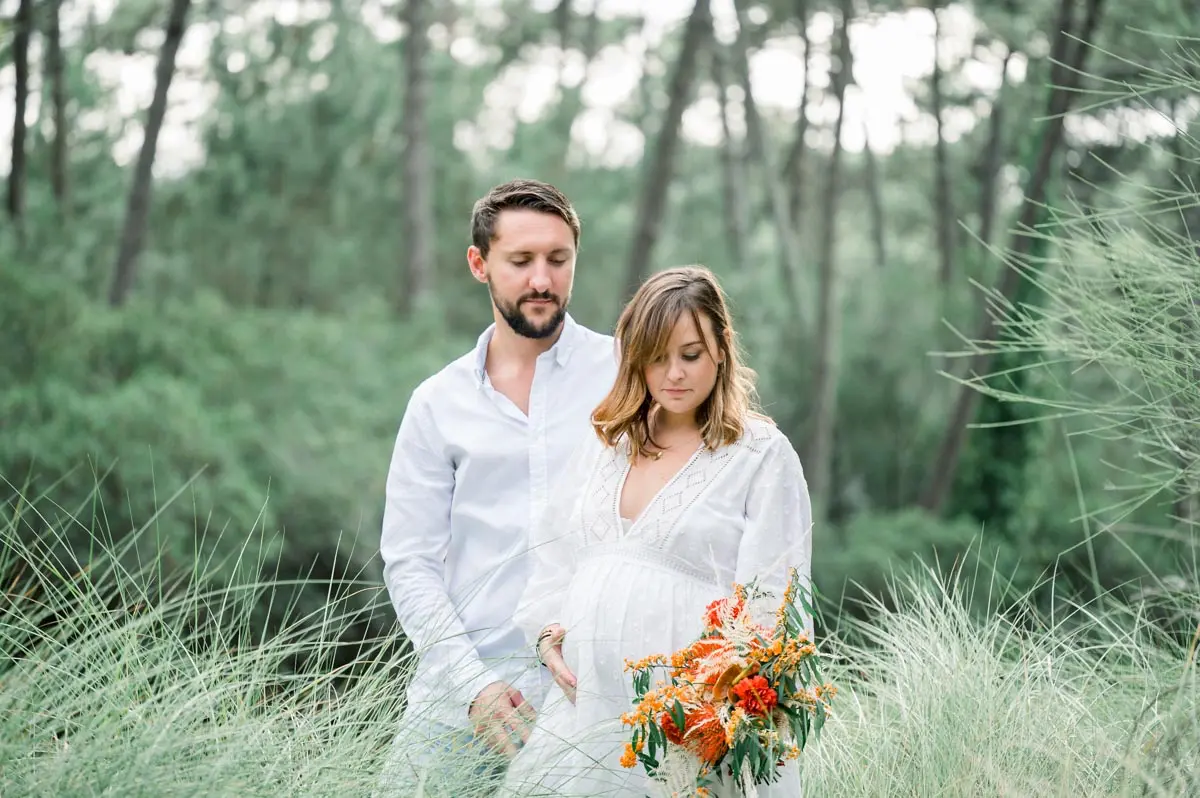 Expectant couple with an orange bouquet in a pine forest on Arcachon Bay