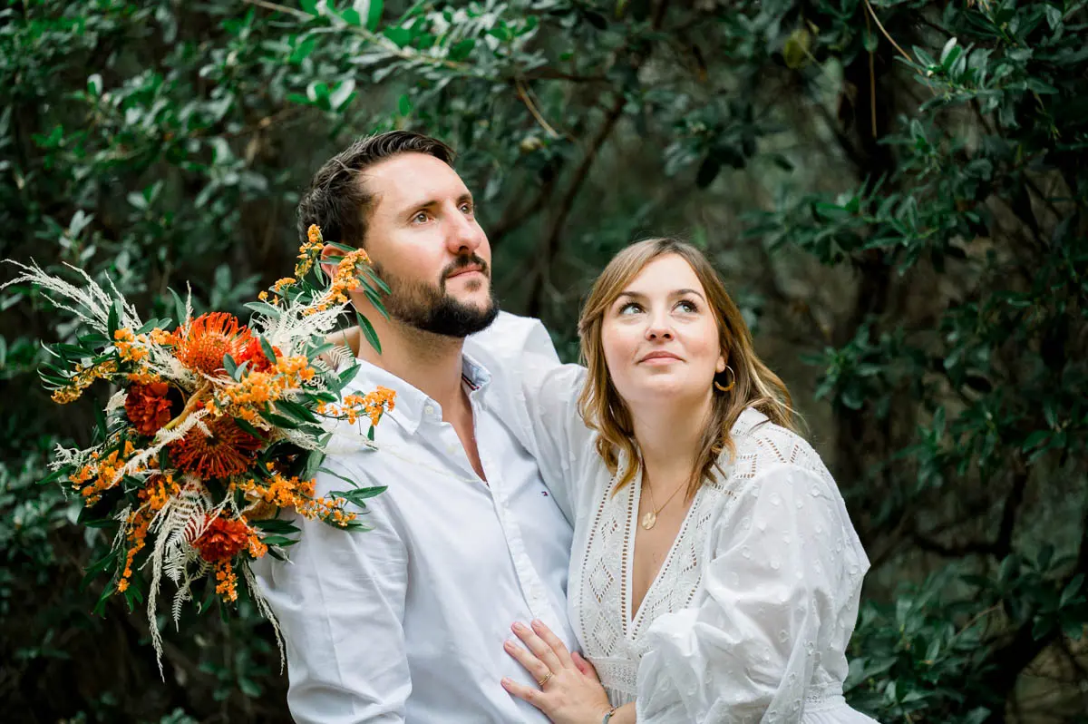 The parents-to-be gaze upwards holding an orange bouquet