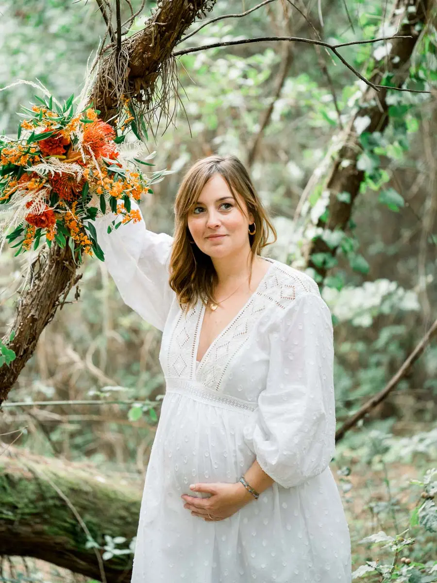 Mum-to-be leaning on a tree with an orange bouquet hanging in its branches