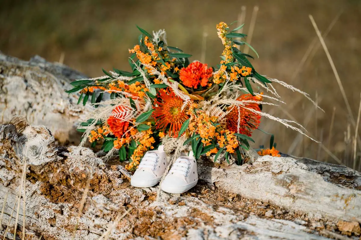 Baby shoes and an orange bouquet laid on a tree trunk