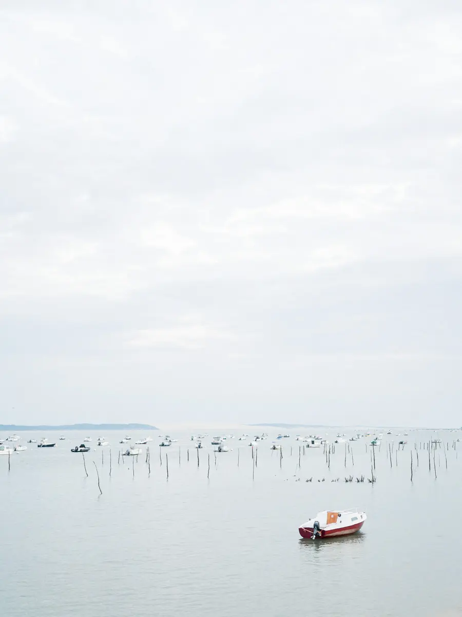 Small red boat and oyster beds on Arcachon Bay on an overcast day