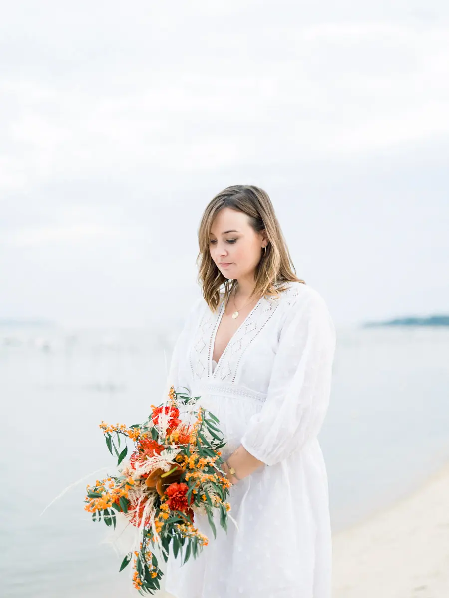 Mum-to-be in a white dress on the beach at Arcachon Bay, bouquet in hand