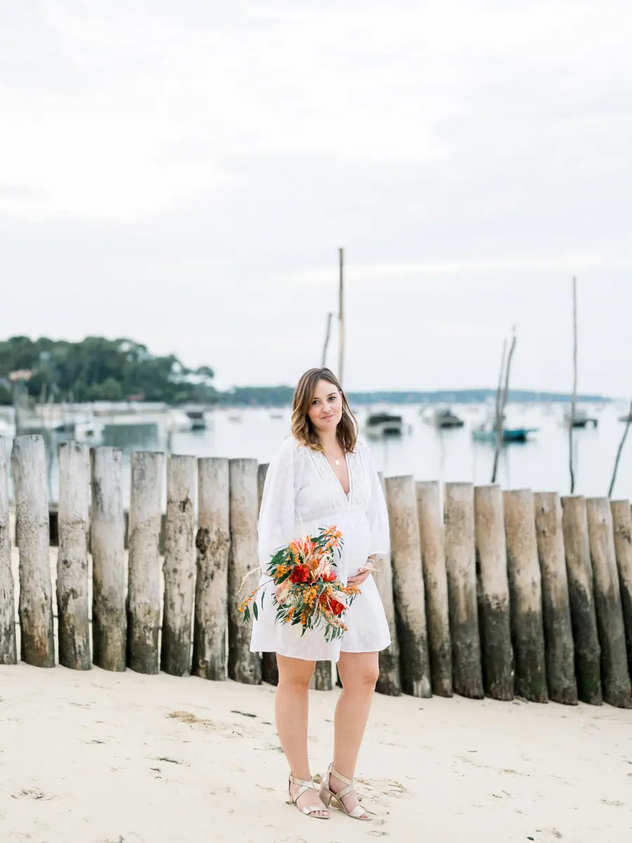 Mum-to-be standing on the beach in front of a row of wooden stakes