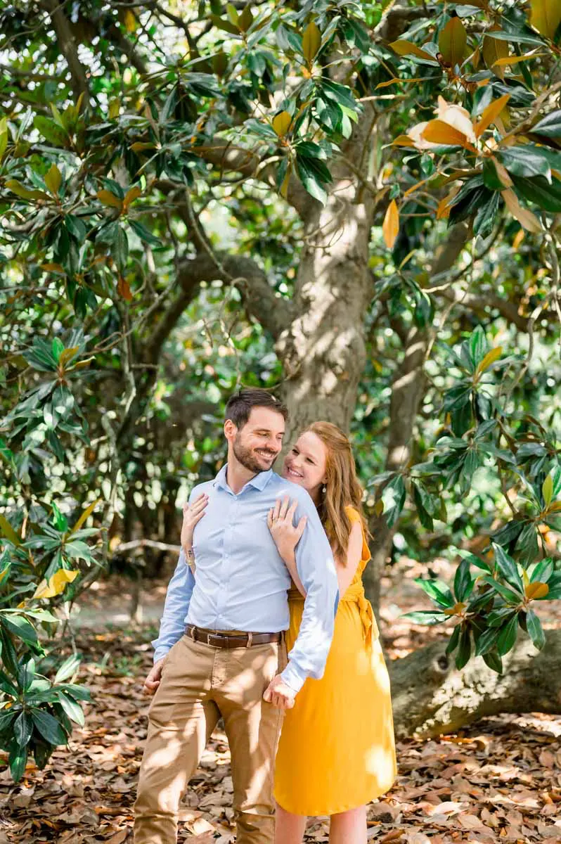 Expectant couple embracing under a large magnolia tree in Parc Bordelais