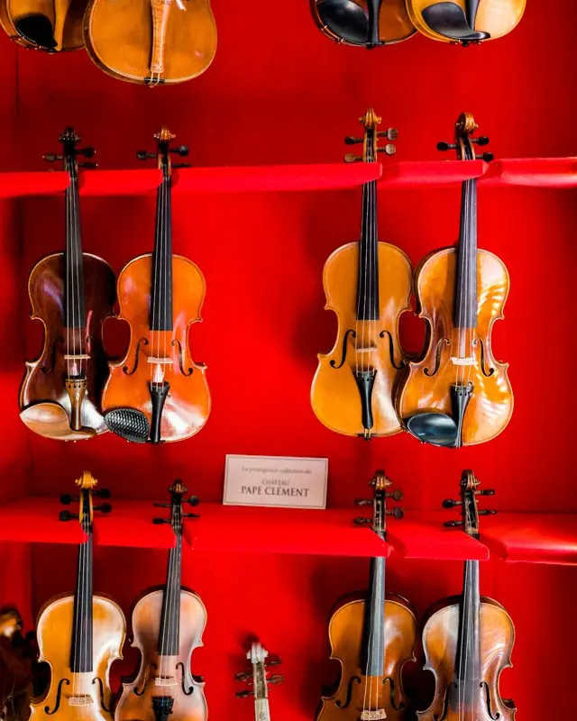 Collection of violins displayed on red shelves at Château Pape Clément