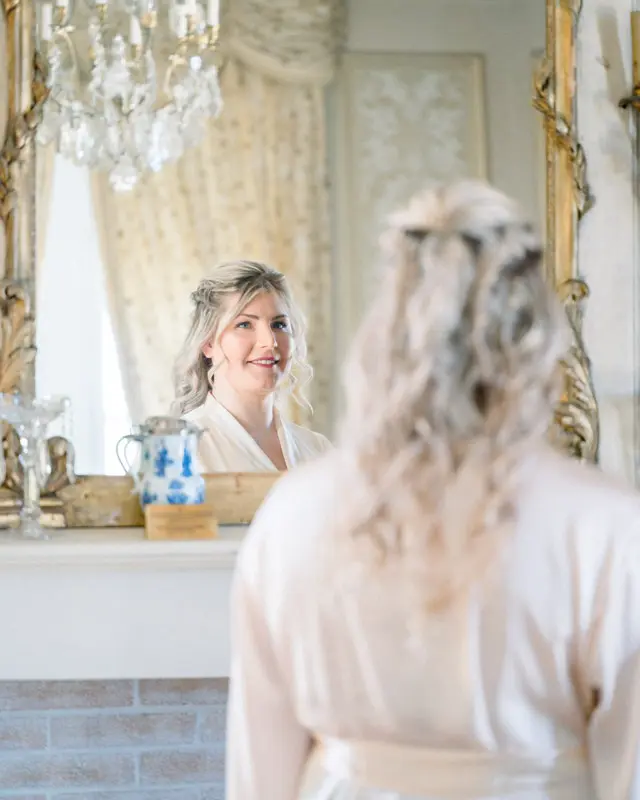 Julie looking into a gilded mirror in a château salon before dressing