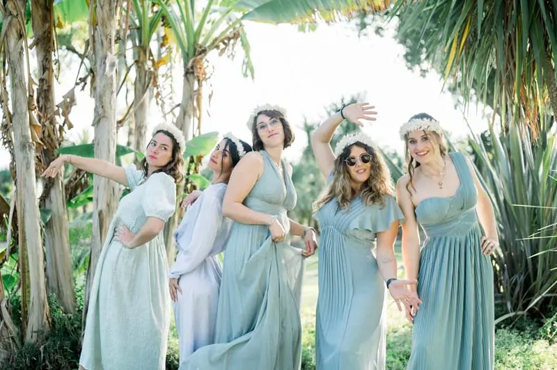 Bridesmaids in sage green dresses striking playful poses under the palms