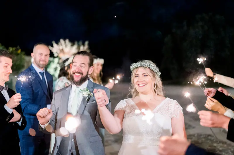 The couple laughing among guests holding sparklers at night