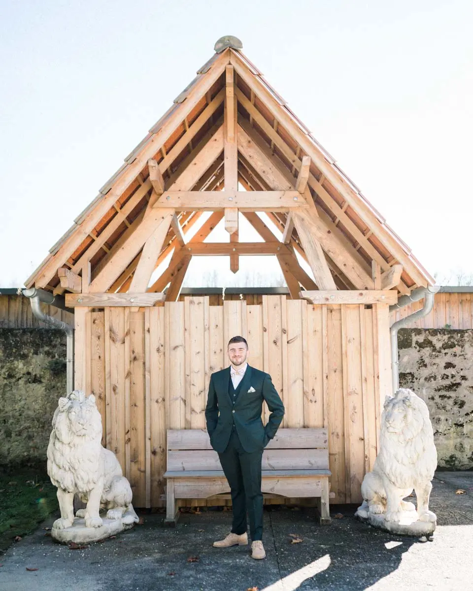 The groom in a green suit under a timber shelter between two stone lions