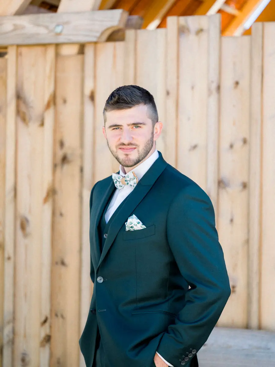 Portrait of the groom in a fir-green suit against timber cladding
