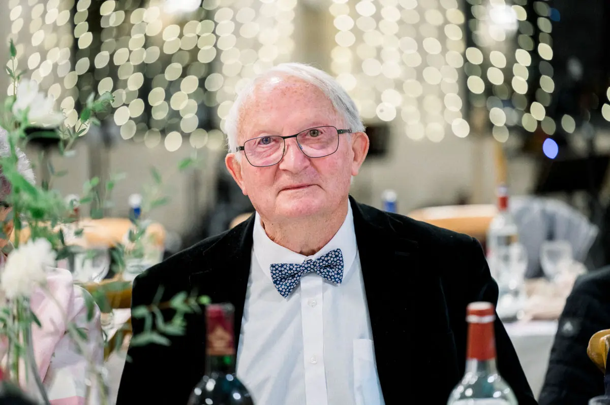 Older guest in a bow tie listening intently during the wedding dinner