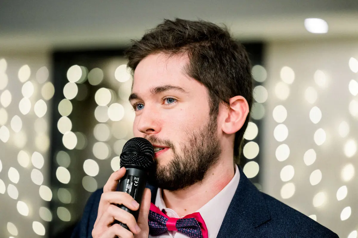 A guest in a pink bow tie giving a speech into the microphone