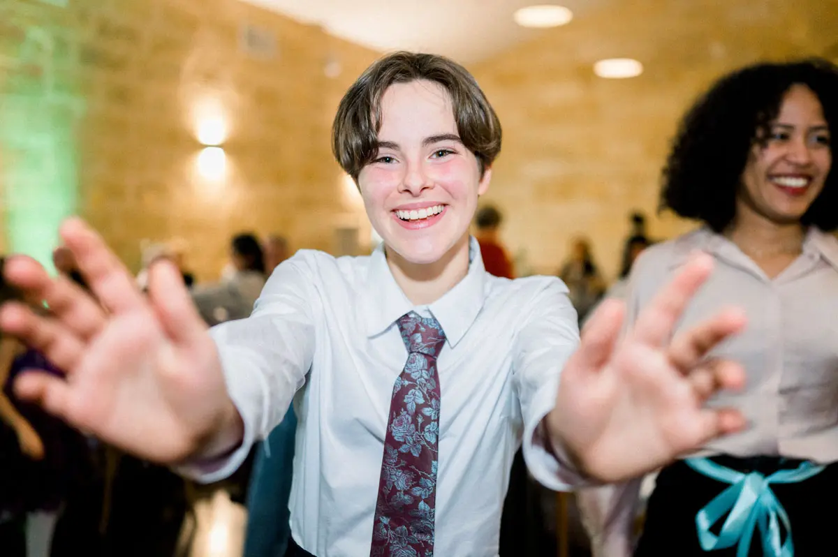 Young guest in a tie dancing with arms stretched towards the camera