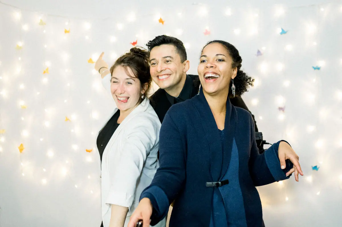 Three guests dancing and laughing in front of a curtain of fairy lights