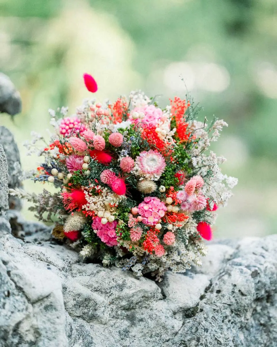 Dried flower bouquet in pink and coral tones resting on a rock