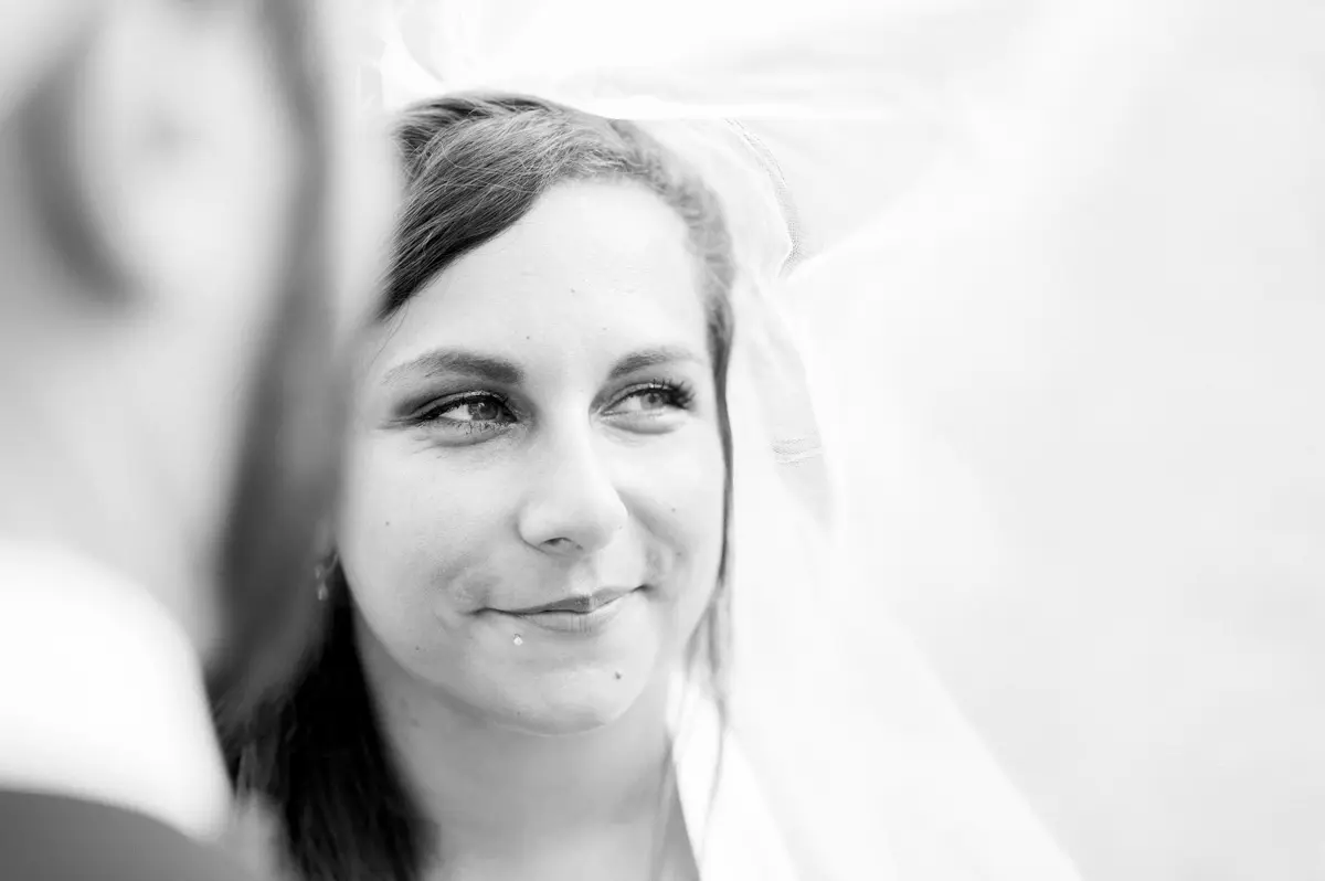 Black and white portrait of the smiling bride beneath her veil