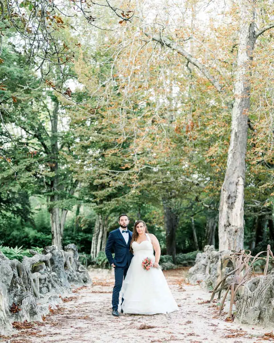 Bride and groom on a sandy path between tall trees in Parc Majolan